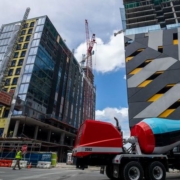 A cement truck is parked in front of some tall buildings.