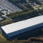 A large warehouse with many cars parked in the lot.